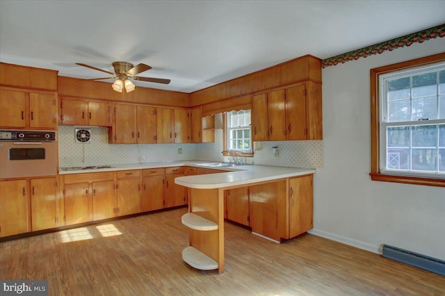 kitchen with baseboard heating, light hardwood / wood-style floors, wall oven, kitchen peninsula, and gas stovetop