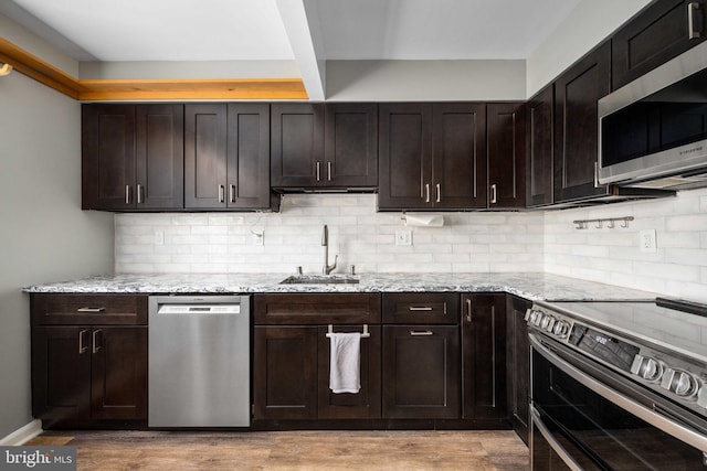 kitchen featuring light stone counters, dark brown cabinetry, appliances with stainless steel finishes, and sink