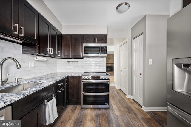 kitchen featuring light stone counters, sink, stainless steel appliances, and dark brown cabinetry