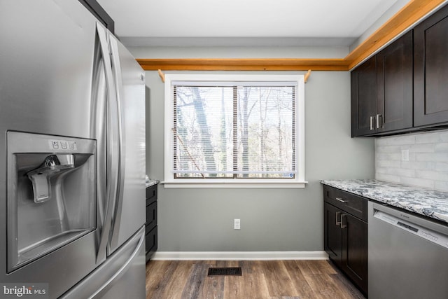 kitchen with dark brown cabinetry, appliances with stainless steel finishes, light stone countertops, and plenty of natural light