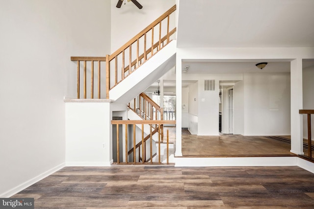 staircase with wood-type flooring, ceiling fan, and a high ceiling