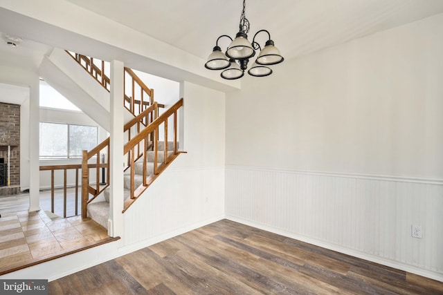 unfurnished dining area featuring an inviting chandelier, wood-type flooring, and a brick fireplace