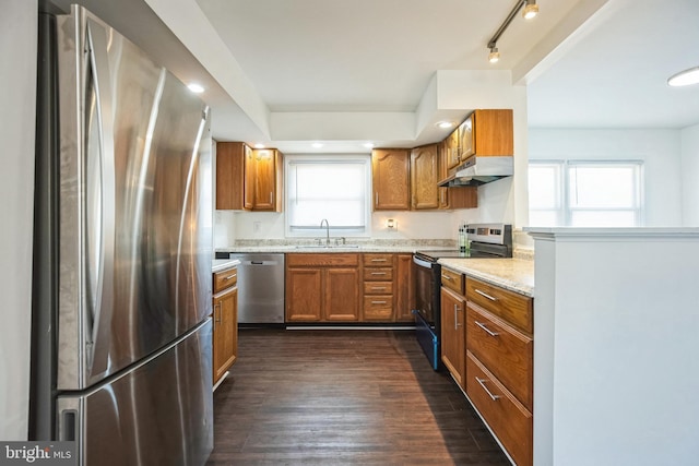 kitchen featuring dark wood-type flooring, sink, light stone counters, track lighting, and appliances with stainless steel finishes