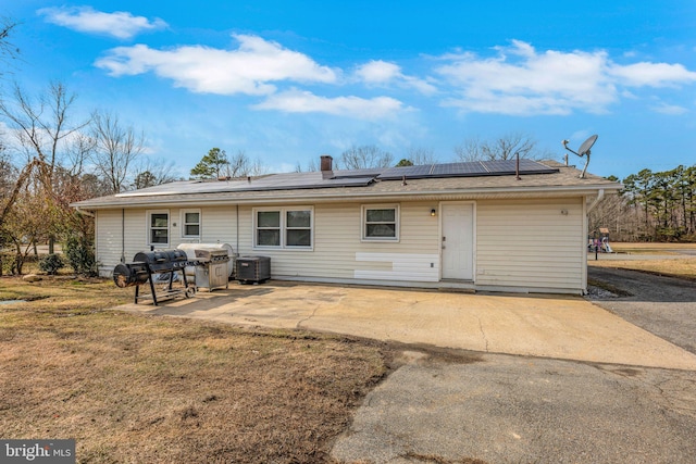 rear view of house with cooling unit, a yard, a patio, and solar panels