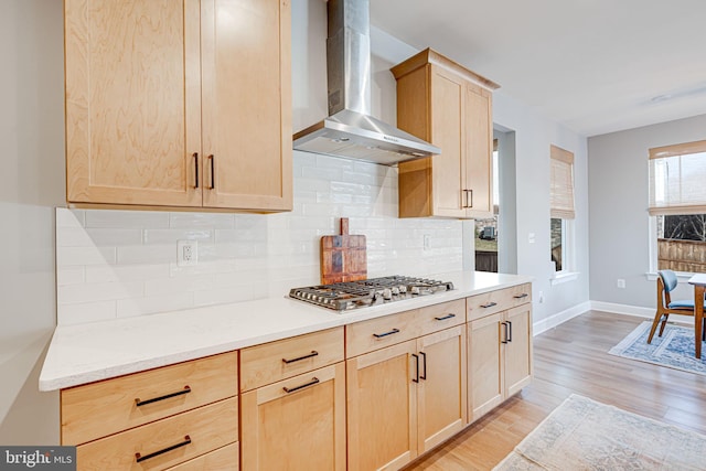 kitchen with baseboards, wall chimney exhaust hood, light brown cabinetry, light wood-type flooring, and stainless steel gas stovetop