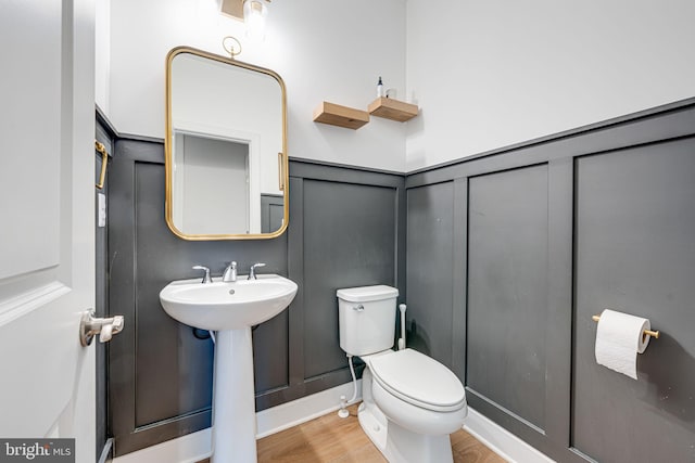 half bathroom featuring wood finished floors, a sink, toilet, and a decorative wall