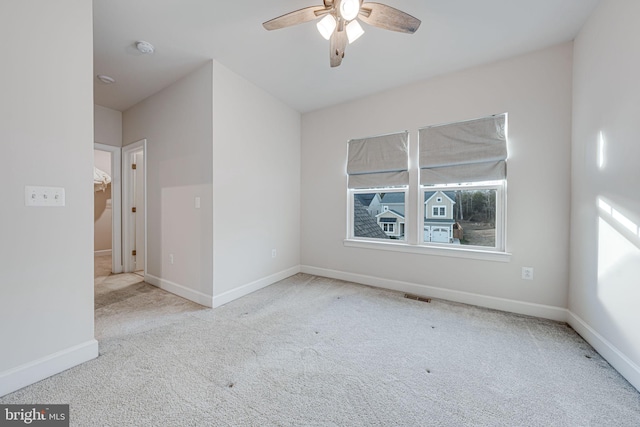 carpeted spare room with ceiling fan, visible vents, and baseboards