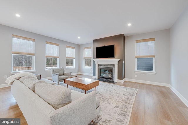 living area featuring recessed lighting, a fireplace with flush hearth, light wood-style flooring, and baseboards