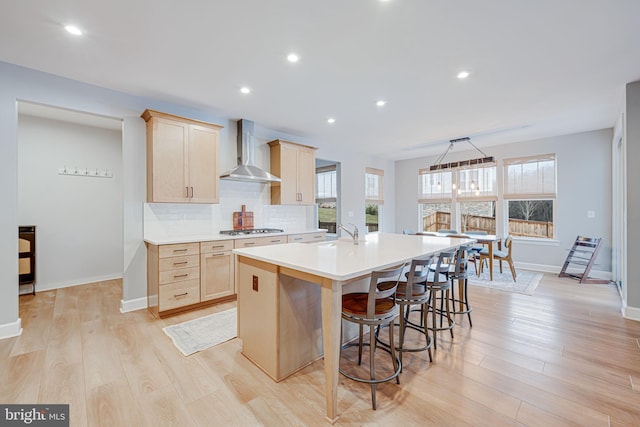 kitchen with light countertops, light brown cabinetry, wall chimney range hood, stainless steel gas cooktop, and backsplash