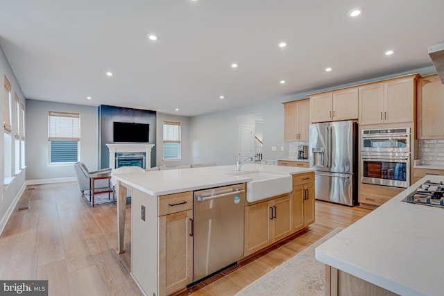 kitchen featuring a fireplace, light wood-style flooring, light brown cabinetry, appliances with stainless steel finishes, and a sink