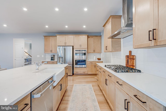 kitchen featuring stainless steel appliances, light brown cabinetry, light wood-style floors, light stone countertops, and wall chimney exhaust hood