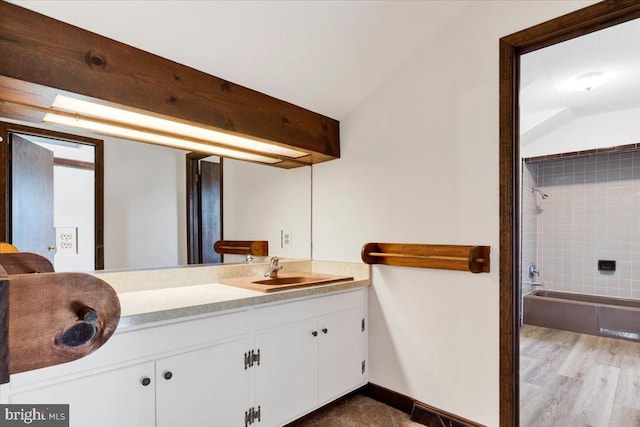 bathroom with tiled shower / bath combo, vanity, lofted ceiling, and wood-type flooring