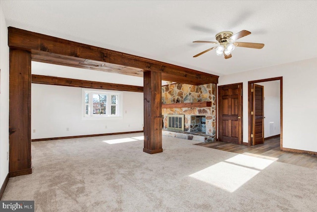 unfurnished living room featuring ceiling fan, a stone fireplace, and light carpet