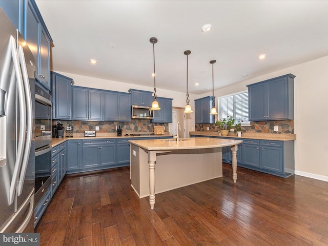 kitchen with blue cabinetry, a breakfast bar area, decorative light fixtures, stainless steel appliances, and a kitchen island with sink