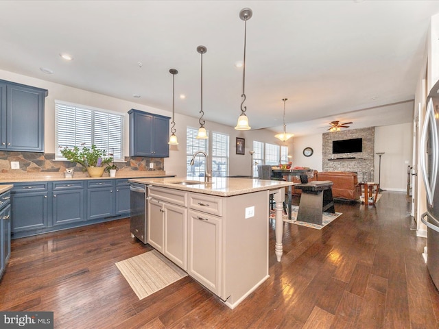 kitchen featuring sink, backsplash, hanging light fixtures, light stone counters, and an island with sink