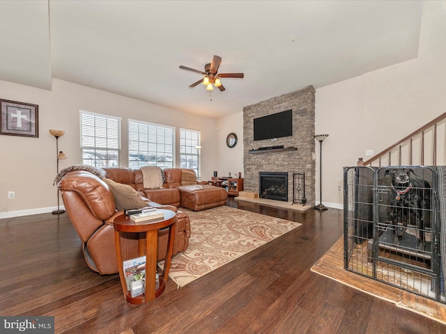 living room with dark wood-type flooring, ceiling fan, and a stone fireplace