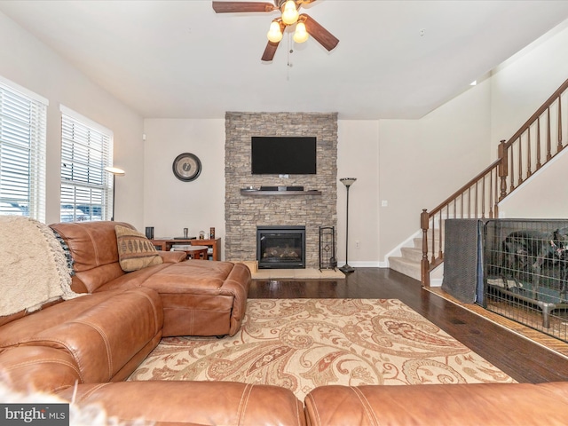 living room featuring a stone fireplace, dark hardwood / wood-style floors, and ceiling fan