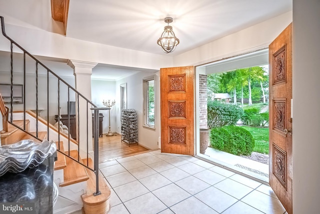 tiled foyer with crown molding, a notable chandelier, and ornate columns