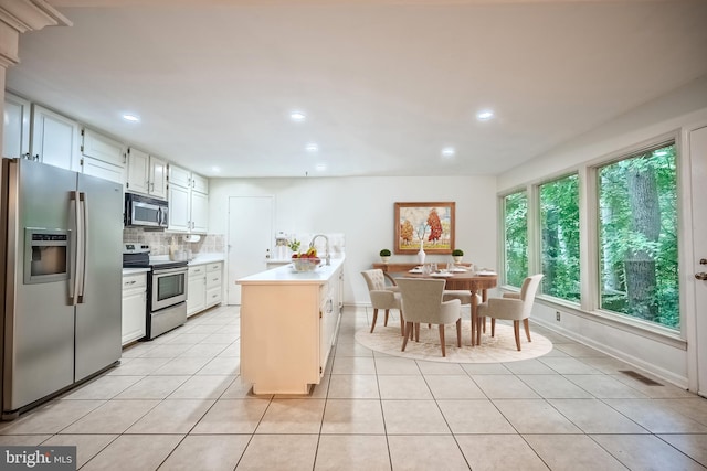 kitchen with a center island, appliances with stainless steel finishes, white cabinetry, light tile patterned floors, and backsplash