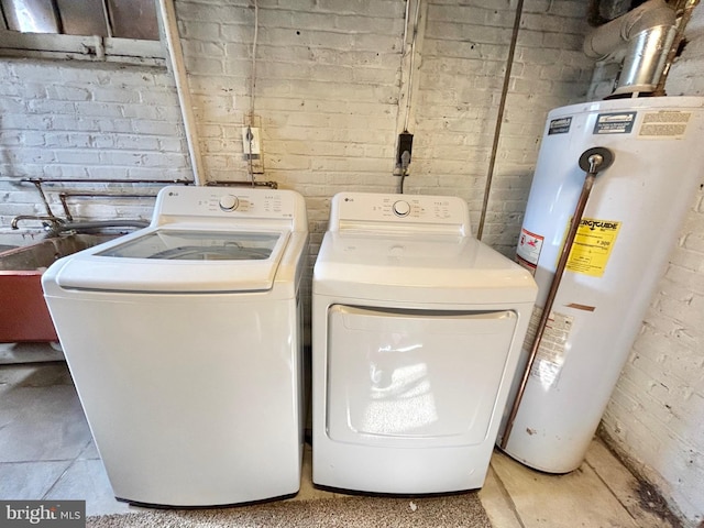 clothes washing area with washer and dryer, water heater, and brick wall