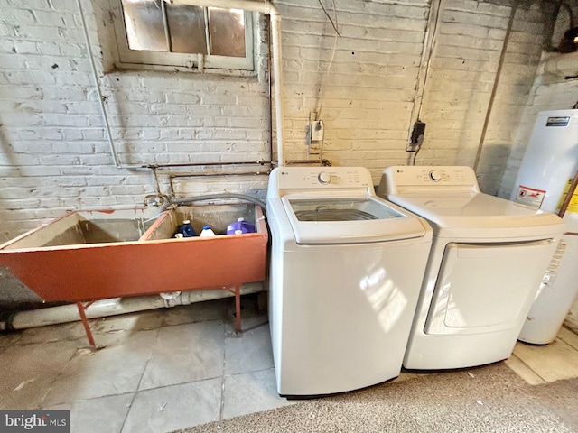 clothes washing area with water heater, washing machine and dryer, and brick wall