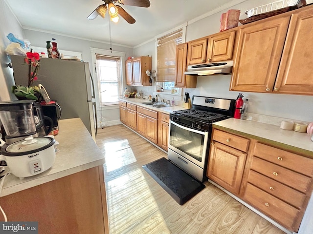 kitchen featuring sink, ornamental molding, ceiling fan, stainless steel gas range oven, and light hardwood / wood-style flooring