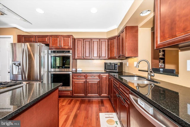 kitchen with sink, hardwood / wood-style flooring, stainless steel appliances, ornamental molding, and dark stone counters