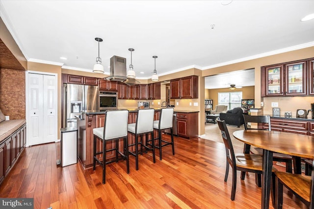 kitchen with pendant lighting, crown molding, a breakfast bar, stainless steel appliances, and island exhaust hood