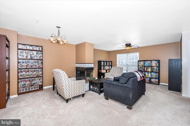 carpeted living room with a tiled fireplace and ceiling fan with notable chandelier