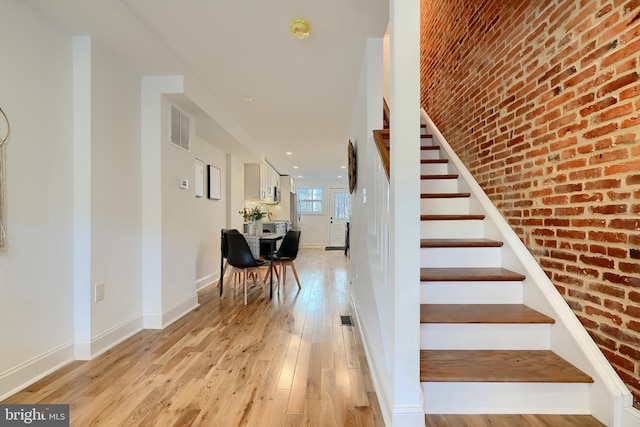 stairs with brick wall and hardwood / wood-style floors