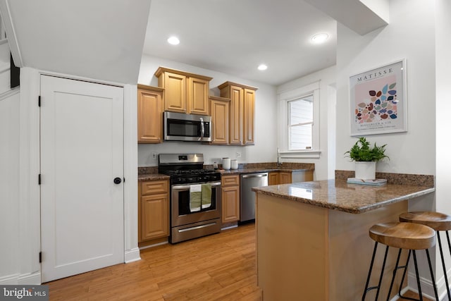 kitchen with appliances with stainless steel finishes, dark stone counters, kitchen peninsula, a breakfast bar, and light hardwood / wood-style flooring