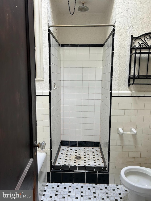 bathroom featuring toilet, tile patterned floors, and a tile shower