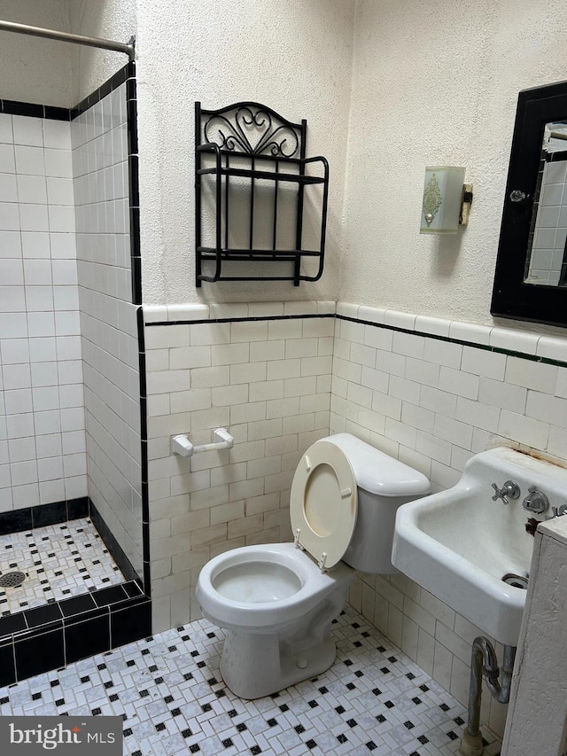 bathroom featuring a tile shower, toilet, tile patterned flooring, and tile walls