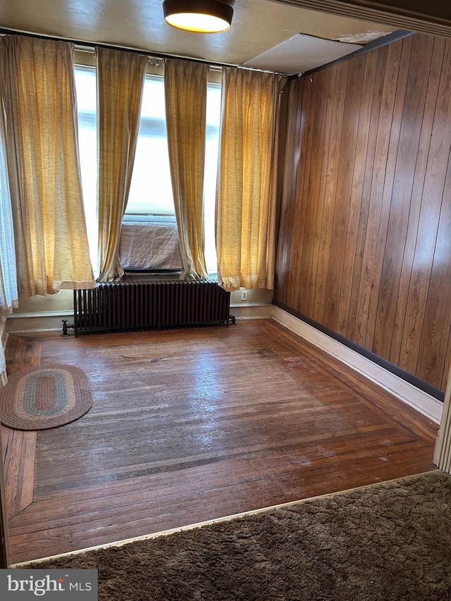 spare room featuring dark hardwood / wood-style floors, radiator, and wood walls