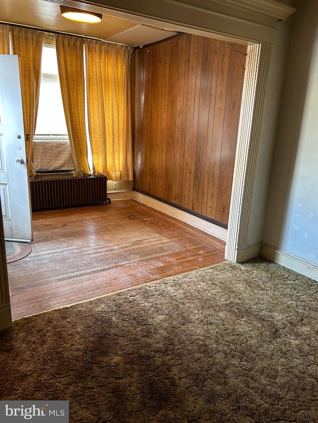 unfurnished room featuring hardwood / wood-style floors, radiator, and wood walls