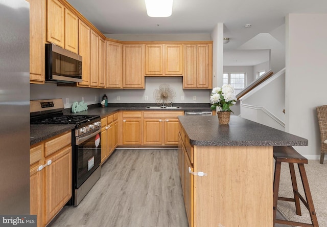 kitchen with a breakfast bar, a center island, light brown cabinets, appliances with stainless steel finishes, and light hardwood / wood-style floors