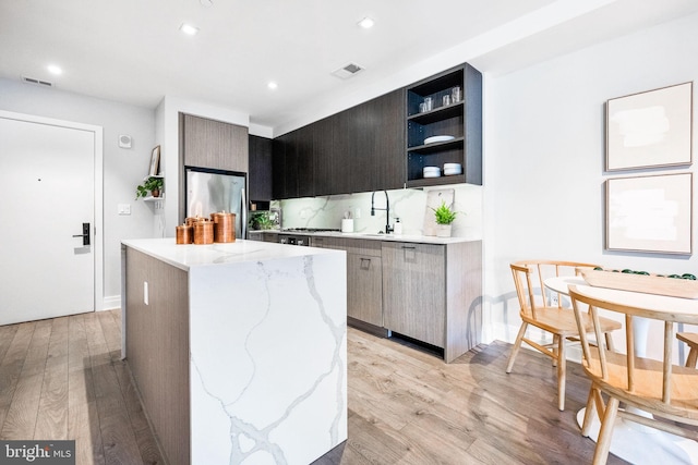 kitchen with light wood-type flooring, a kitchen island, sink, stainless steel refrigerator, and light stone counters