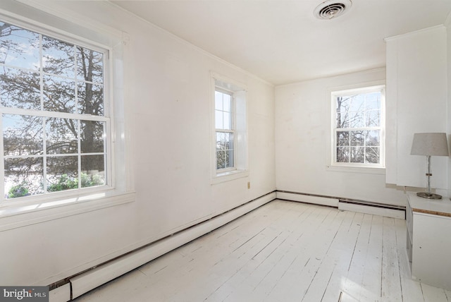 spare room featuring crown molding, a healthy amount of sunlight, light hardwood / wood-style floors, and a baseboard heating unit