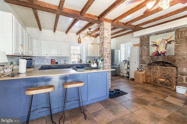 kitchen with a fireplace, white cabinets, a kitchen breakfast bar, decorative backsplash, and ceiling fan