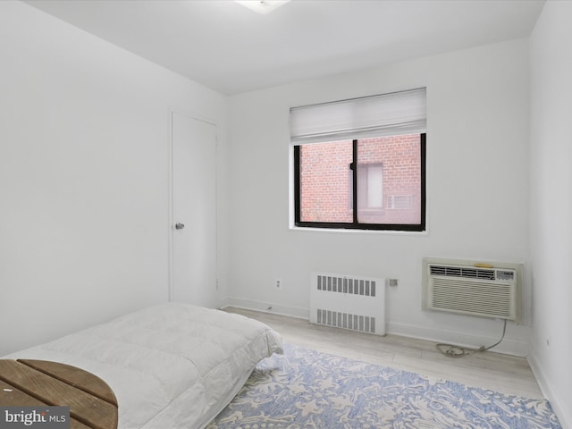 bedroom with radiator, a wall unit AC, and light wood-type flooring