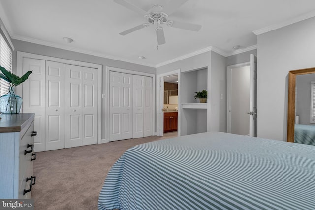 bedroom with crown molding, ensuite bath, light carpet, multiple closets, and ceiling fan