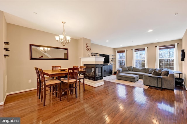 dining space with a multi sided fireplace, hardwood / wood-style floors, and a notable chandelier