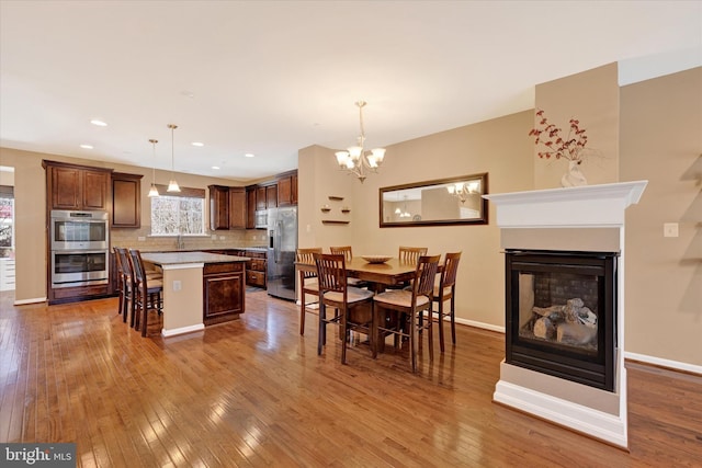 dining room with hardwood / wood-style floors, a notable chandelier, sink, and a multi sided fireplace