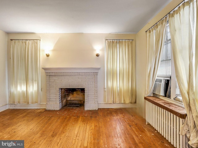 unfurnished living room with radiator, cooling unit, hardwood / wood-style floors, and a fireplace