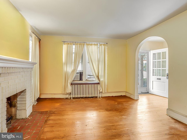 unfurnished living room featuring wood-type flooring, radiator heating unit, and a fireplace