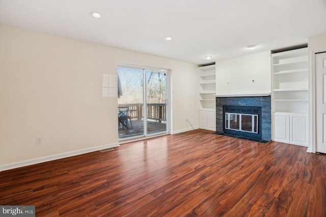 unfurnished living room with a stone fireplace, dark wood-type flooring, and built in shelves