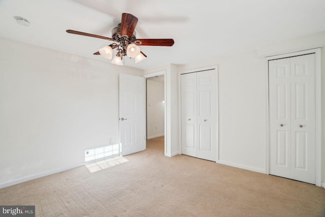 unfurnished bedroom featuring ceiling fan, light colored carpet, and two closets