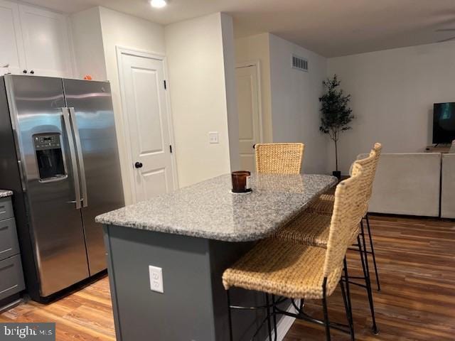 kitchen featuring a kitchen breakfast bar, stainless steel refrigerator with ice dispenser, light hardwood / wood-style flooring, gray cabinetry, and a center island