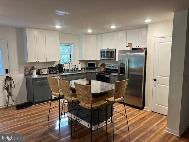 kitchen featuring appliances with stainless steel finishes, white cabinetry, gray cabinetry, dark stone countertops, and a breakfast bar area