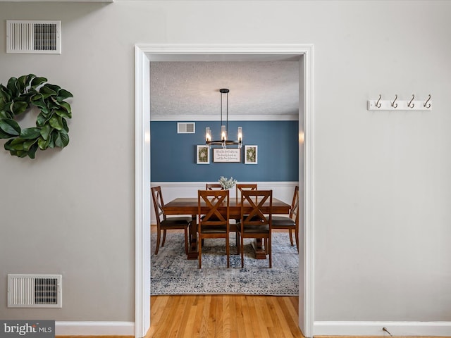 dining area with hardwood / wood-style flooring, a textured ceiling, an inviting chandelier, and ornamental molding